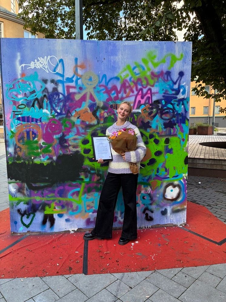 Dansstipendiat My Primbom med diplom och blombukett framför graffitivägg vid Kulturkvarteret