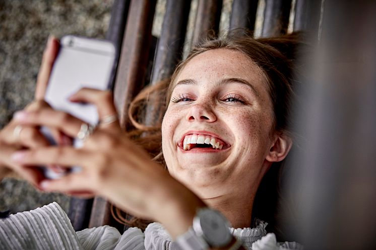Laughing young woman lying on a bench using cell phone.jpg