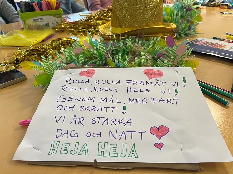 Ett bord med en handtextad skylt med en hejaramsa, hattar i guld och färglada girlanger.