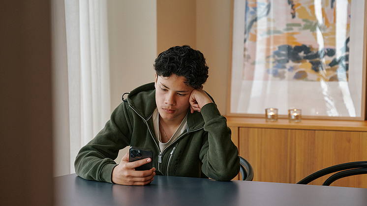 Tonårspojke sitter vi ett bord med en mobiltelefon i handen. Han använder Allie, ett digitalt verktyg för samordning.