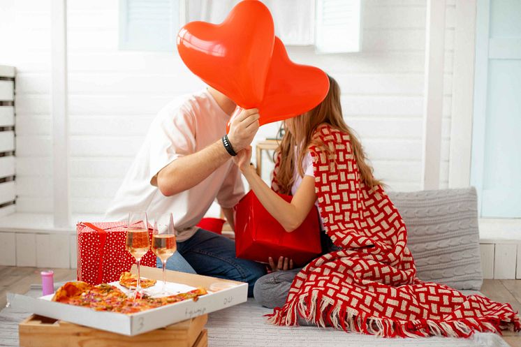 young-couple-celebrates-valentine-s-day-they-kiss-closed-with-red-airy-hearts-as-symbol-holiday-romantic-atmosphere-with-wine-pizza-lots-gifts-infinitely-happy-together.jpg