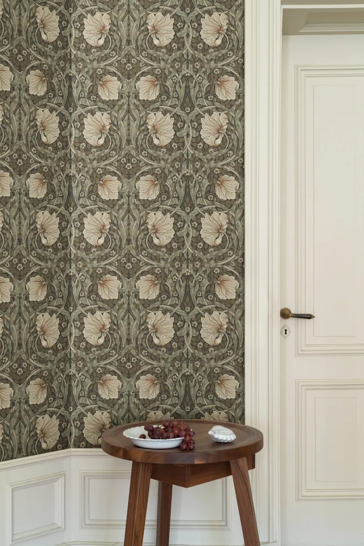 Detaljrik tapet med stiliserade blommor och blad i dämpade gröna och beige toner, intill en vit spegeldörr och ett träbord.