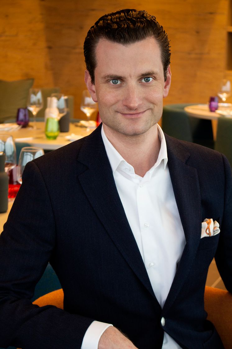 Portrait von Patrick Rausch. Er sitzt im THE ROOF Restaurant.