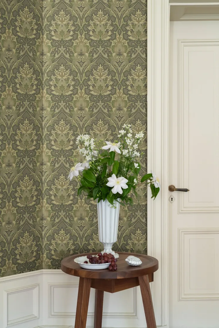 Detaljmönstrad tapet i dämpade gröna och beige toner, vit spegeldörr och träbord med vas fylld av vita blommor.