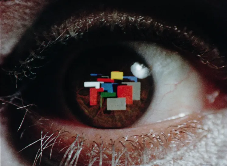 Stillbild från konstnären Peter Nesrles film Sightseeing. Närbild på ett öga där olikfärgade block speglas i iris.