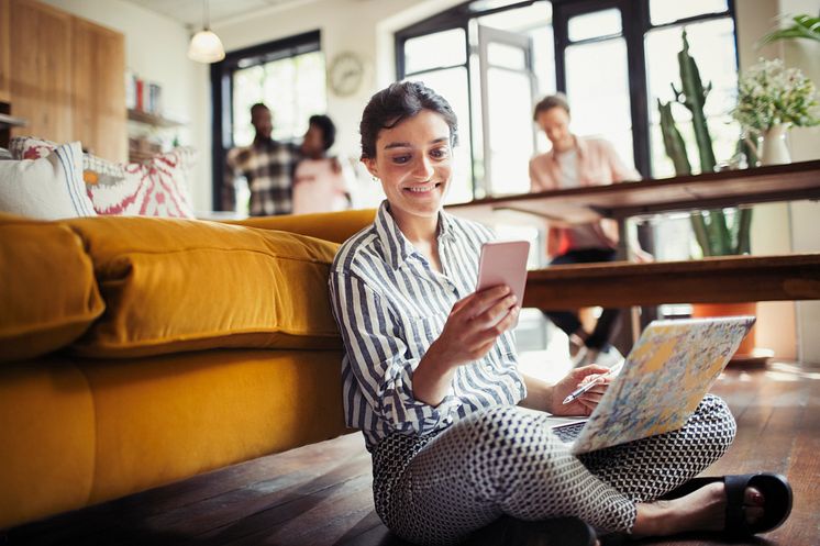 Smiling young woman using laptop and texting with smartphone_Paul Bradbury_GettyImages-922710980