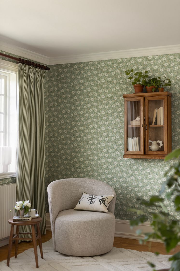 Tapet med blommor och blad i beige, vitt och dov turkos i läshörna med grå fåtölj.
