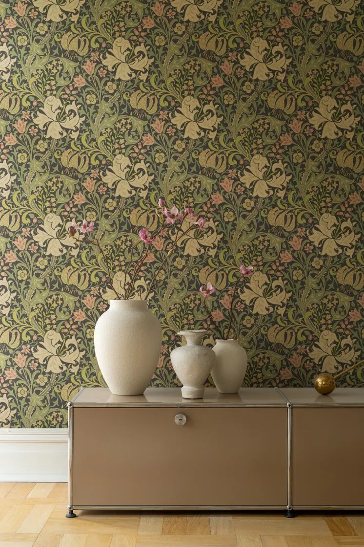 Detaljrik blommönstrad tapet i gröna, rosa och cremefärgade toner med beige skåp och dekorativa vaser.