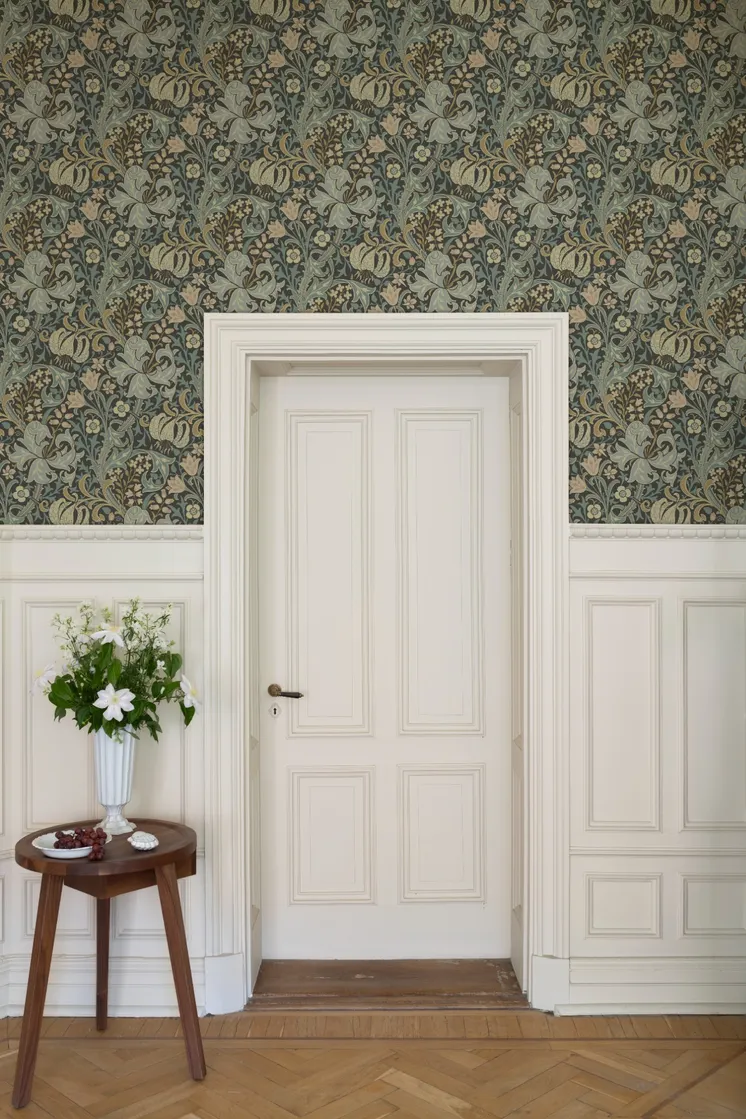 Klassisk interiör med detaljrik blommönstrad tapet i dämpade gröna och blå toner, vit bröstpanel och spegeldörr.