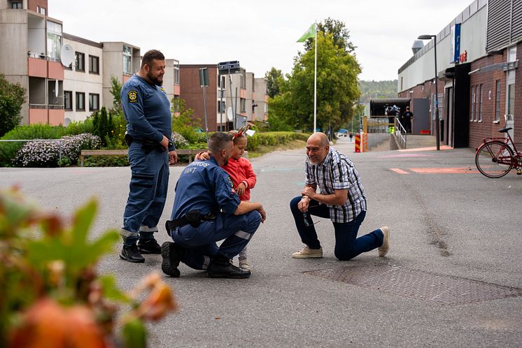 Två ordningsvakter i uniform pratar med ett barn och en vuxen i Fittja.jpg