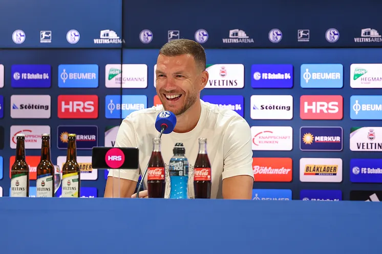Edin Džeko lacht auf dem Podium in der Pressekonferenz.