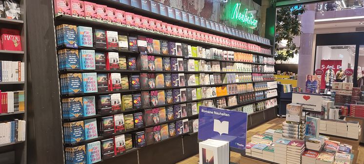 Regalwand mit Roman-Neuheiten in der Thalia Buchhandlung PlusCity Pasching, vorn ein Büchertisch mit Büchern.
