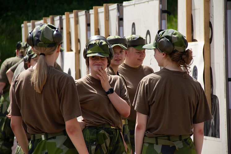 Unga kvinnor i uniform  med keps och hörselkåpor på huvudet.