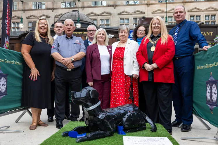 A group of men and women smiling behind a metal sculpture of a dog. 