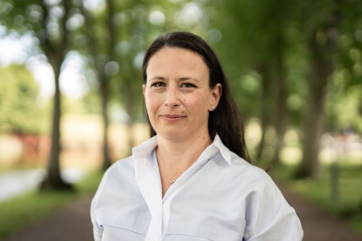 Kvinna i vit blus i en allé med gröna träd