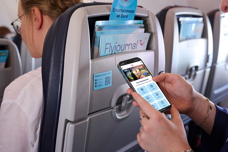 Matkustaja käyttää älypuhelinta lennolla; istuintaskussa Flyjournal-lehti ja digitaalinen  viihdetarjonta 