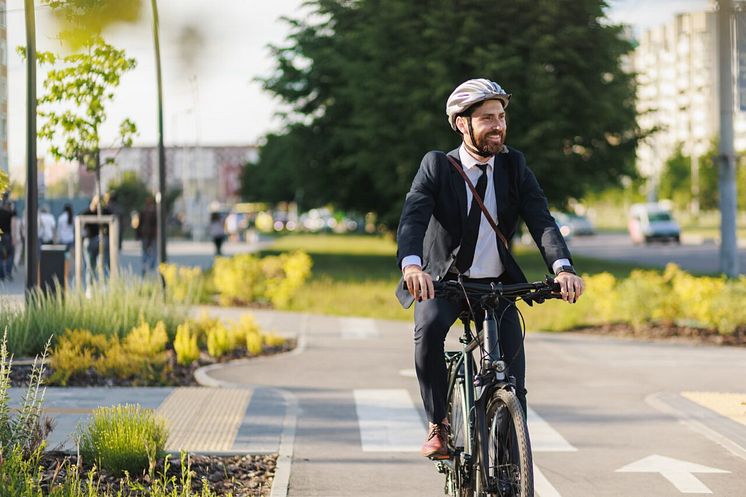 Man med hjälm cyklar med kostym i stan. 