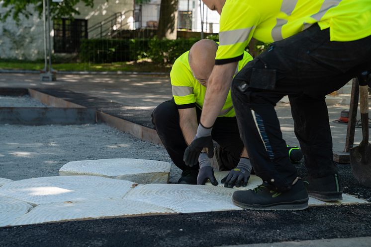 To menn kledd i synlighetstøy står på huk og monterer heksagon-moduler. 