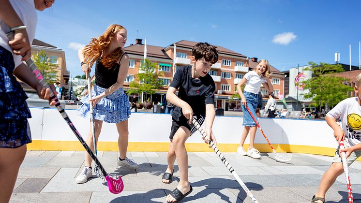 Några barn spelar innebany i en innebandyrink på ett torg.