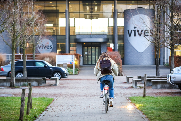 Vives-Hogeschool-Studierende radelt auf Campus mit Vives Logo.png