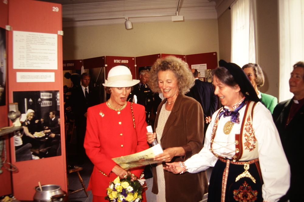 Tre festkledde kvinner i en utstilling på et museum, den ene er dronningen av Norge.