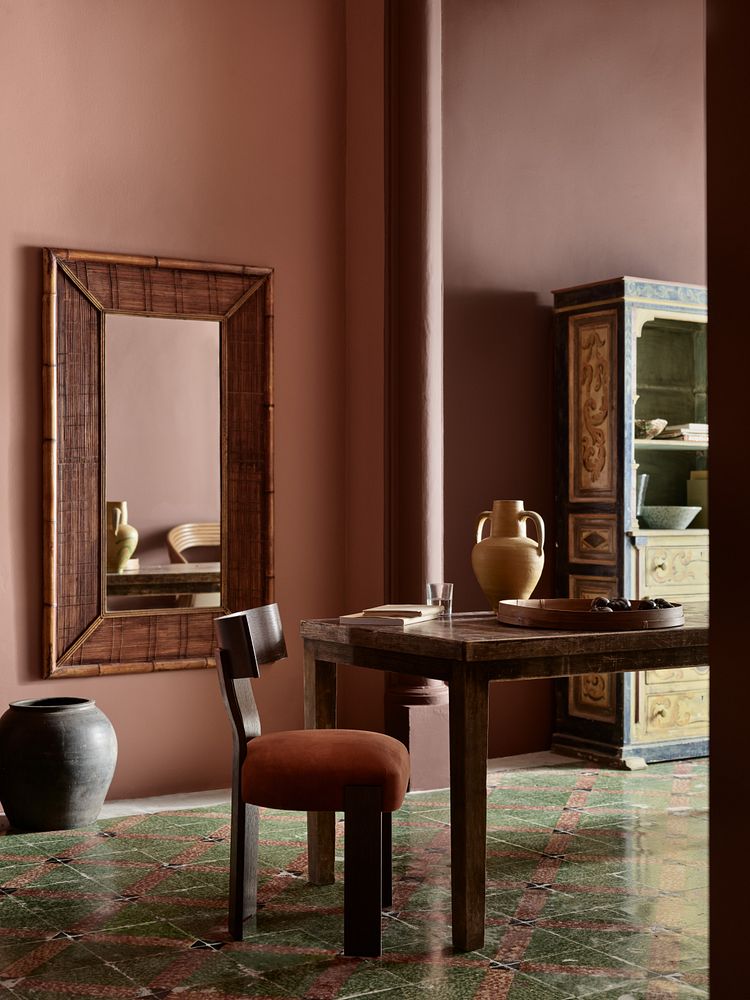 Stue i rustikk stil med spisebord, stort speil på veggen. Veggene er malt i brente rødtoner Amber Red og veggen til høyre med fargen Kilim, begge fra Jotun.