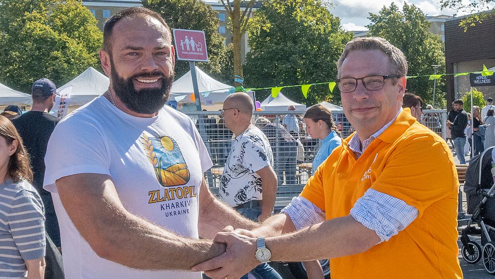Två män skakar hand inför en folksamling.