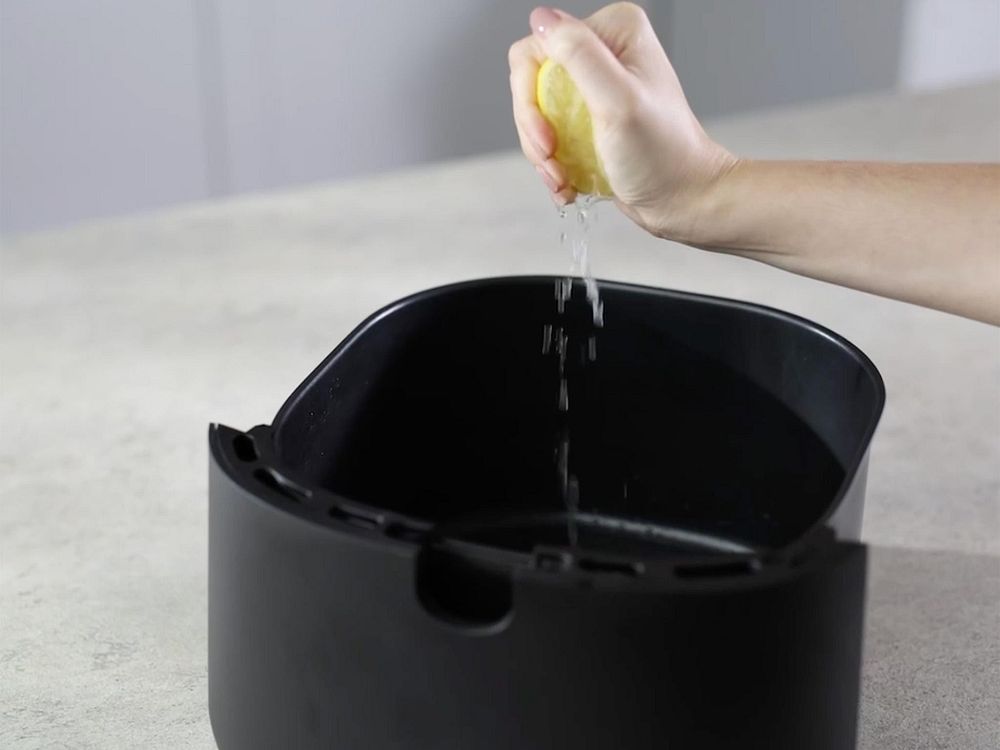 En hand pressar citronsaft för att göra rent insidan på en Philips Airfryer korg