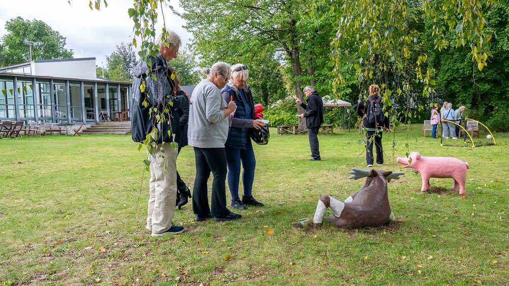 En grupp människor som står i en trädgård vid ett par statyer av djur.