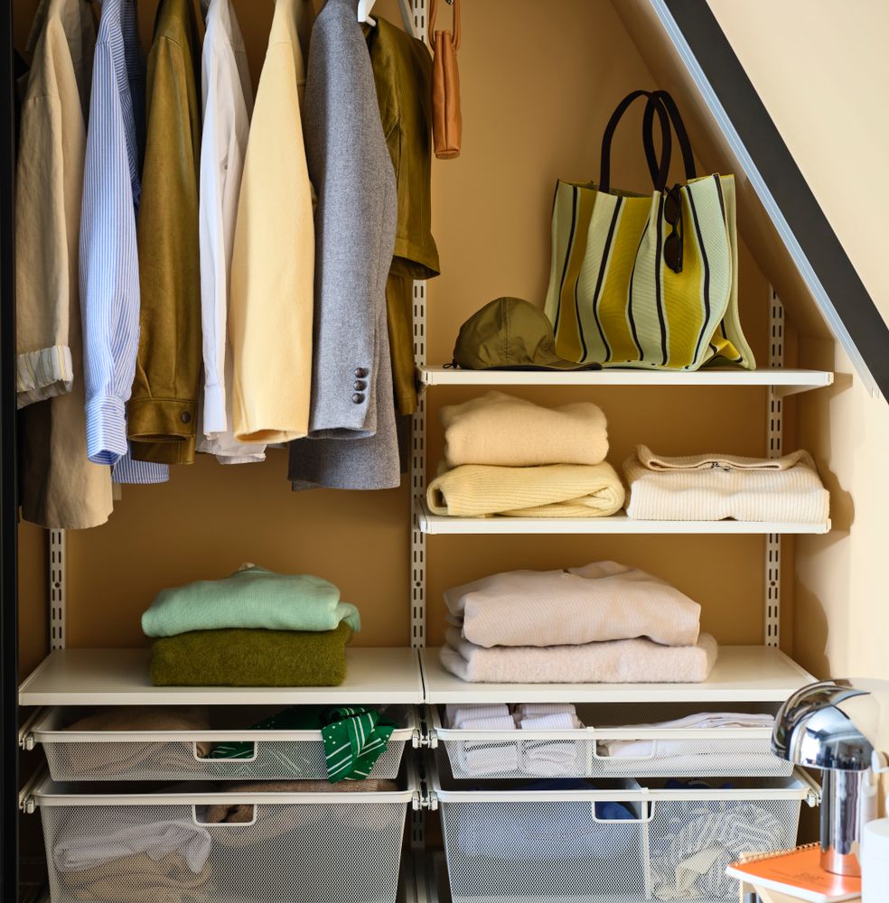 Offene Aufbewahrungslösung von Elfa unter einer Dachschräge mit hängender Kleidung, gefalteten Strickwaren, Taschen und Körben.