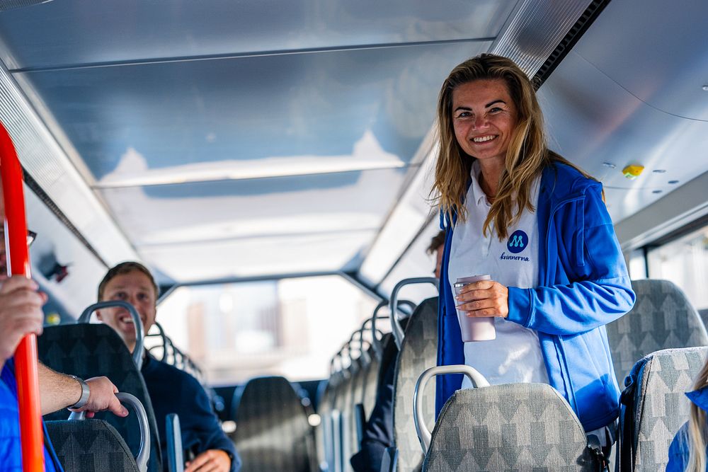 En kvinna håller på att sätta sig på en buss. Hon ler stort.