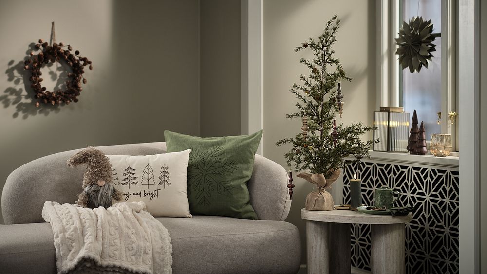 Ett vardagsrum som är dekorerat för julen med krans på väggen och en pappstjärna i fönstret. I soffan är det kuddar med julmotiv och i bakgrunden står en liten konstgran.