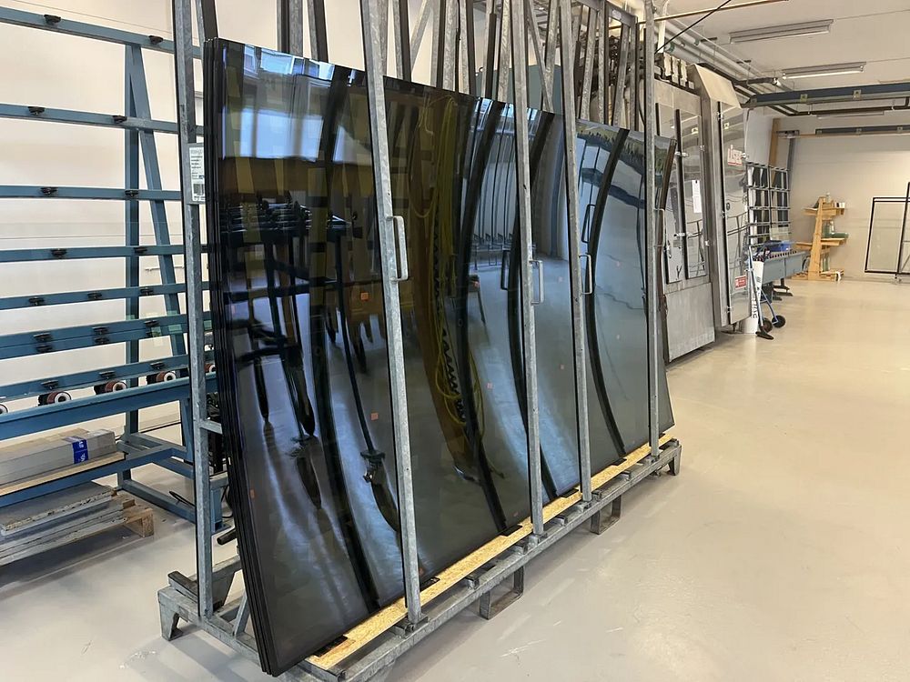 Böjda glaskassetter med mörk toning står uppradade i en produktionsmiljö. Glaspanelerna är färdiga för leverans och installation i fasaden till Boverkets nya huvudkontor.