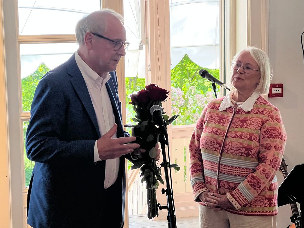 En eldre mann med en rosebukett i hånden, og en kvinne på en scene.
