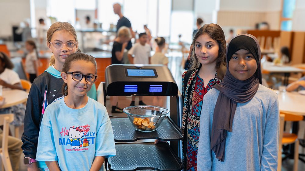 En grupp unga flickor står bredvid varandra intill en måltidsrobot.