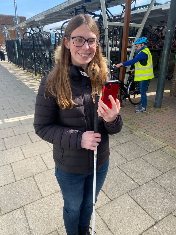 Woman holding a mobility cane uses her phone and the Aira app to navigate a station