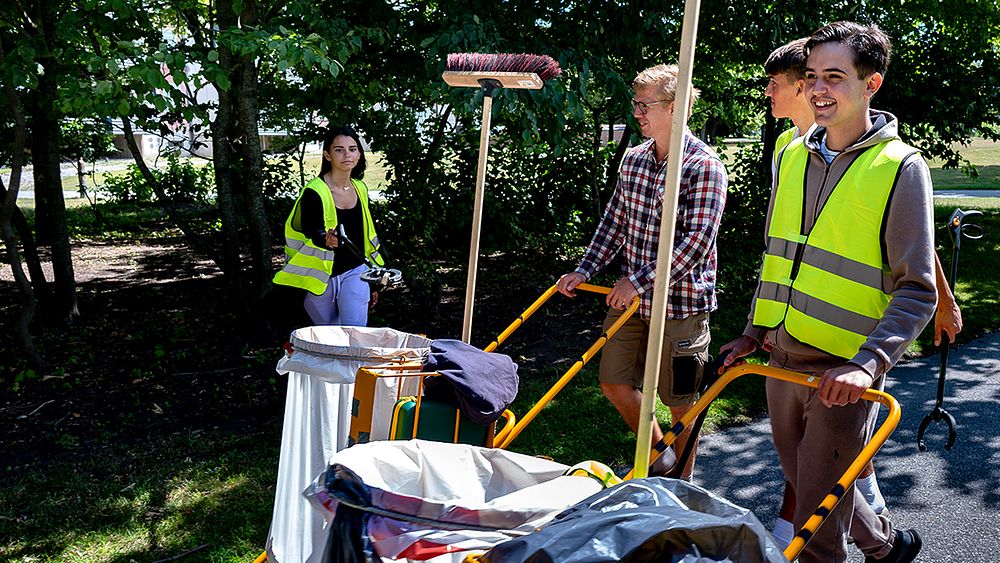 Några personer som går på en väg med en vagn med sopsäck.