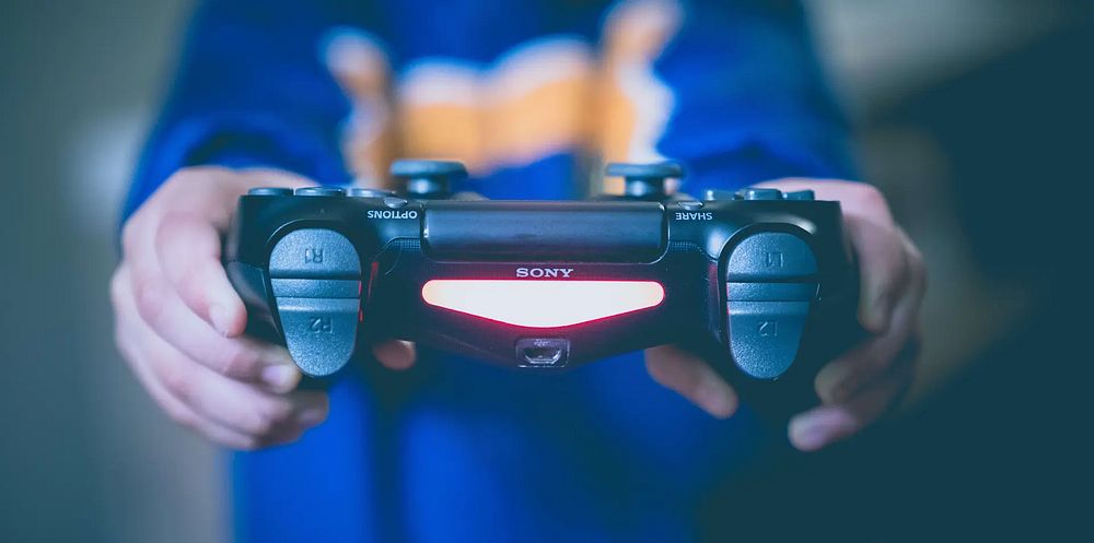 En person håller en Sony-spelkontroll mot tittaren. Fyra knappar på handkontrollens axel är i fokus. Foto.