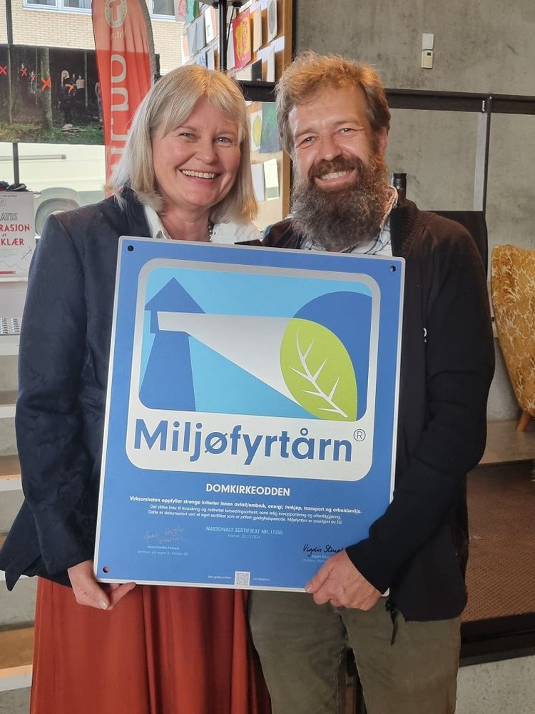En kvinne og en mann som holder et skilt med Miljøfyrtårnlogo.